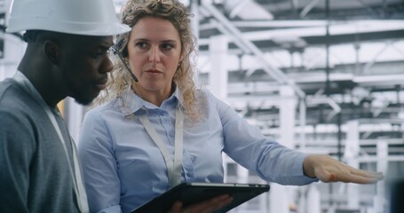 Technical Team Performing on Site Inspection in Modern Automated Factory. Female Manager Uses Tablet Review Digital Schematics While Guiding Male Engineer. Mobile Technology Integration in Industrial