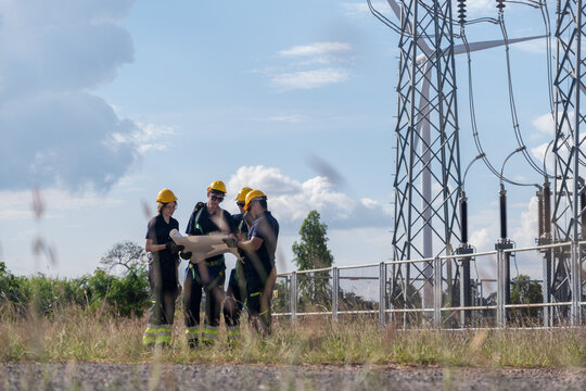 Engineers discuss plans at electrical substation during sunny day near power lines