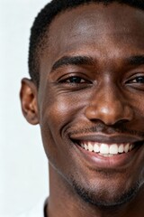 Obraz premium A happy close-up portrait of a young black man with warm skin and a bright smile against a white wall.