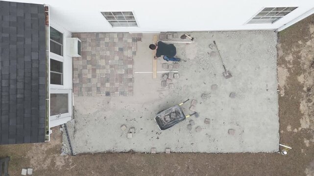 Overhead drone shots of man working on his backyard paver patio doing a DIY construction project. 