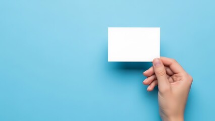 A hand holding a blank white square paper on a light blue background