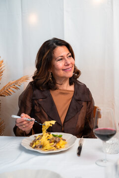 Vertical lifestyle portrait of elegant woman enjoying homemade pasta dinner with red wine