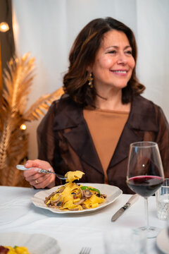 Smiling mature woman enjoying homemade Italian pasta and red wine at elegant home dinner