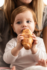 Young child enjoying a croissant while sitting with an adult in a cozy indoor setting during morning