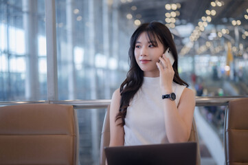 Fototapeta premium Asian businesswoman using laptop and phone while waiting at airport
