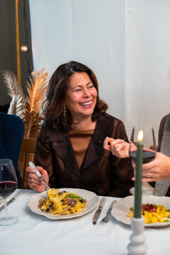 Smiling woman enjoying Italian pasta and red wine during cozy dinner with friends