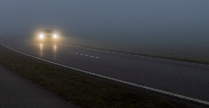 Scheinwerfer eines Autos im dichten Nebel auf nasser Landstra&szlig;e bei Nacht