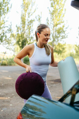 Woman removing yoga equipment from car trunk preparing for outdoor practice