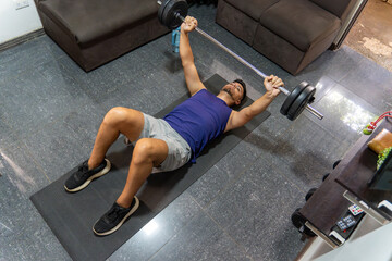 Young adult male doing strength training with a loaded barbell on a fitness mat in a home living space