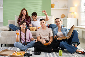 Group of teenagers playing video game and having snacks at home