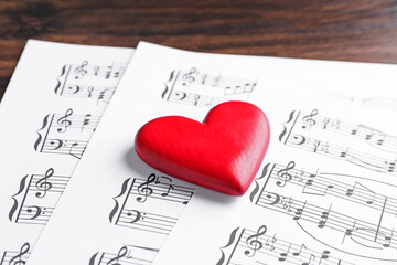 Heart figure and paper sheets with music notes on wooden table, closeup