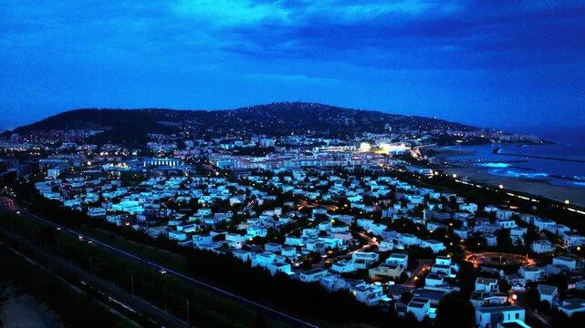 Aerial drone footage of S&egrave;te city at night, featuring illuminated urban landscape, harbor lights, and Mediterranean coastal atmosphere in southern France.
