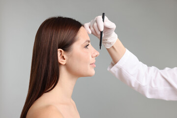 Doctor drawing marks on patient's face for plastic surgery operation against grey background,...