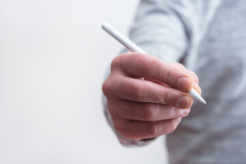 Close up of male hand holding white stylus pen against clean white background. Concept for digital drawing, design, writing and technology.