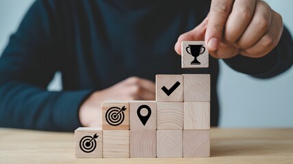 Person placing a wooden block with a trophy on of a stack of blocks with target, location, and checkmark symbols