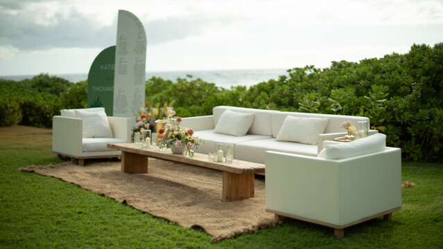 An outdoor couch and chairs in an elegant setting aganist the ocean in Hawaii. 