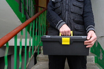 handyman holding a black tool box in a residential building hallway