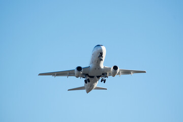 Fototapeta premium White Commercial Airplane Ascending into Clear Blue Sky Right After Airport Takeoff. White Passenger Plane Soaring Through Sunny Blue Sky – Air Travel and Vacation Concept