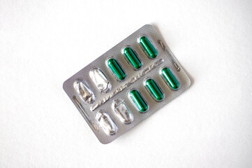 Semi-empty metal blister pack with green capsules isolated on white background. Metal blister for capsules