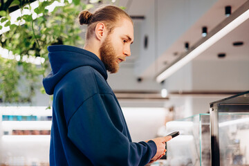 Young man in blue hoodie choosing at cafe display window.