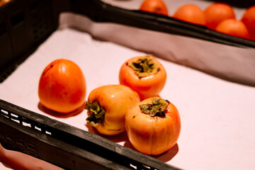 Fresh persimmons displayed in a cardboard box for sale at a market.