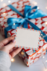 Blank Christmas card in female hand over blurred festive gift.