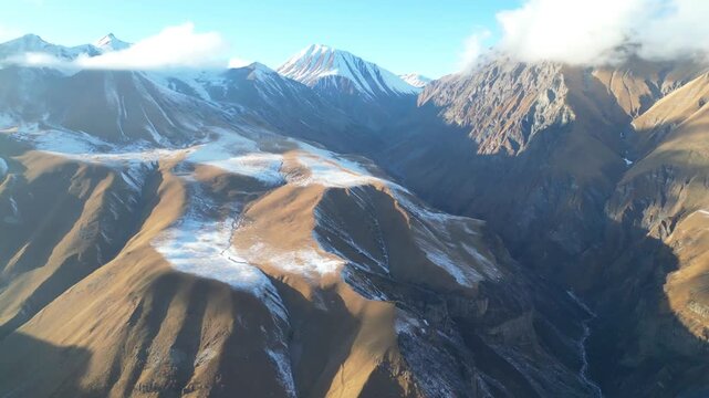 Early winter mountains under clear sunlight. 4K drone footage shows Georgian highlands lightly covered with snow, revealing dramatic natural scenery during a bright and calm day.