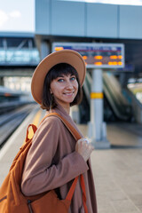 Girl with a backpack. beautiful and young girl in a hat at the station. A young woman in a coat and hat stands on the station platform.