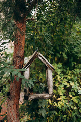 A wooden bird feeder attached to a tree trunk surrounded by lush green leaves.