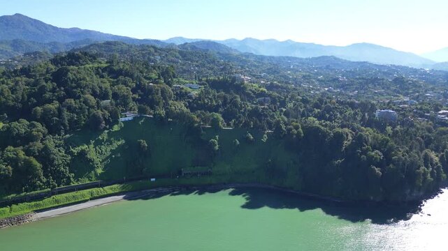 Lush green botanical garden on Black Sea coast in Batumi Georgia. 4K drone footage shows dense evergreen vegetation along a sunny shoreline with vivid colors and calm coastal atmosphere.