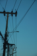 Concrete utility pole with messy electric wires and telecommunication cables against a clear blue sky background.