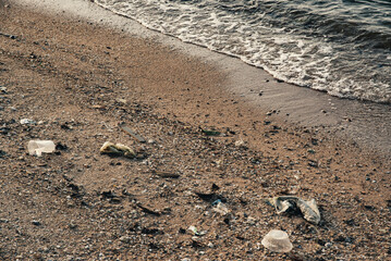 Plastic containers, foam cups, and various garbage scattered on the sand at the seaside. Environmental pollution and marine debris problem.