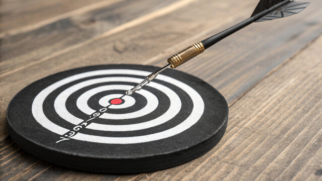 High-angle close-up of a dart hitting the bullseye on a black and white target board over a rustic wooden surface, conceptualizing success, precision, and business achievement.
