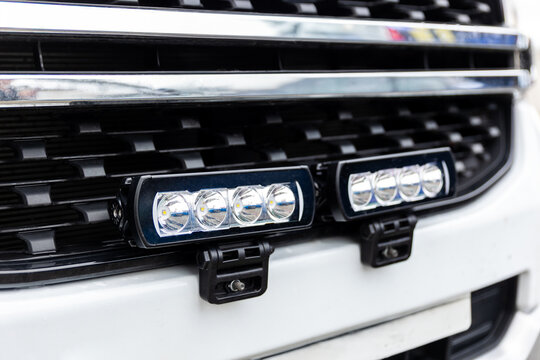 Closeup of vehicle grille with integrated LED strobe lights mounted on bumper, showing modern emergency lighting system for unmarked patrol or service car. Automotive safety equipment visible