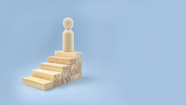 Single wooden figure standing on stacked blocks representing personal growth, achievement, career progress, and self development concept.