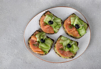 Sandwiches with salted salmon, black olives and cucumber on gray background