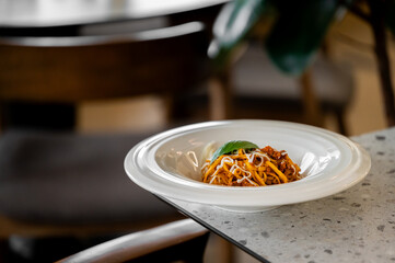 A close-up shot of a plate of delicious spaghetti bolognese with a single basil leaf garnish,...