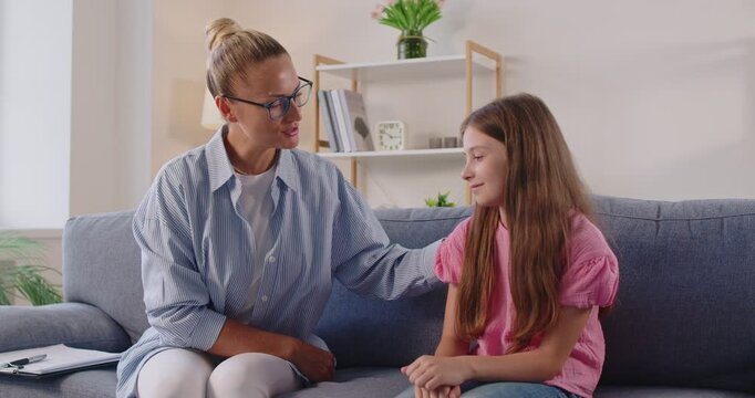 Positive child therapy session from counselor at home. Psychologist holding hand on girls shoulder with smile to build trust and open communication. Friendly dialogue of therapist and listening kid