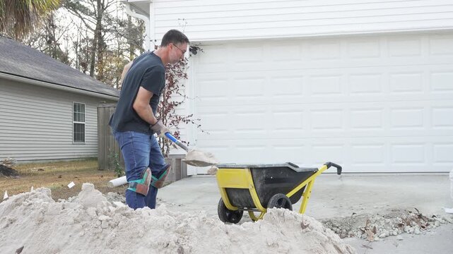 Man shoveling sand into wheelbarrow for DIY project at his home