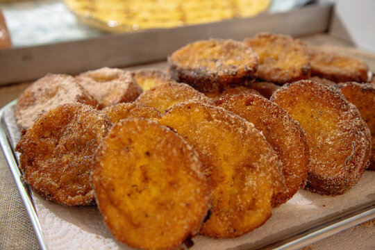 A festive kitchen counter displays traditional Portuguese Christmas desserts, with a tray of cinnamon sugar rabanadas in the foreground and homemade leite creme and aletria cooling in glass dishes beh
