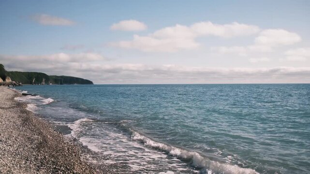 Gentle waves rolling onto a pebble beach on the Black Sea coast in Tuapse, Russia during spring. Calm seaside landscape with fresh air, soft light, and peaceful coastal atmosphere