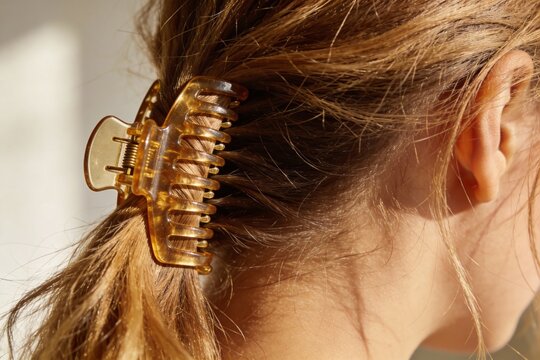 Rear view of woman's long light brown hair styled in low ponytail with oversized tortoiseshell claw clip in soft natural light