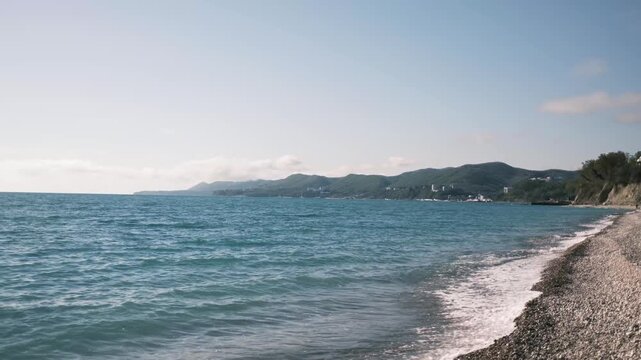 Gentle waves rolling onto a pebble beach on the Black Sea coast in Tuapse, Russia during spring. Calm seaside landscape with fresh air, soft light, and peaceful coastal atmosphere