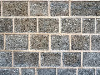 Rough textured surface of a granite stone wall with visible mortar lines