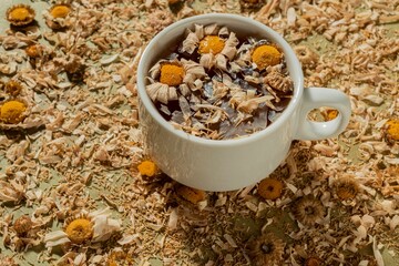 Dry chamomile flowers- tea time. Cup on yellow floral background