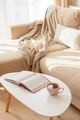 Cozy living room with a book and tea on a beige couch. Soft focus