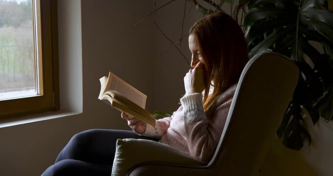 A middle-aged woman immersed in reading in a cosy setting. Intellectual pleasure. Intellectual pleasure.