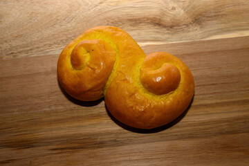Fresh sweet bread is sitting on a wooden surface. The bread has a unique swirl shape and bright yellow color. It was made in a kitchen, showing signs of recent baking