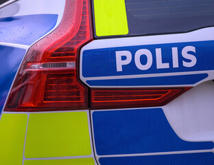 A police vehicle is parked in a rainy setting. The vehicle has bright reflective markings for visibility. Water droplets are present on the surface, adding to the scene