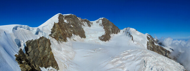 Panorama of Alpine glaciers and snow covered peaks with steep ridges and high altitude terrain. Mountain environment showing ice fields, climate conditions, rugged geology, European Alps landscape, na